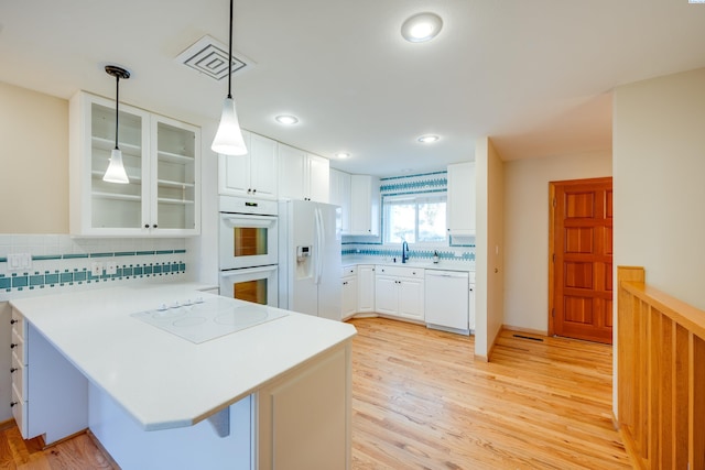 kitchen featuring light countertops, visible vents, glass insert cabinets, white appliances, and a peninsula