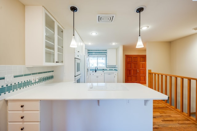 kitchen featuring a breakfast bar area, a peninsula, white appliances, light countertops, and glass insert cabinets