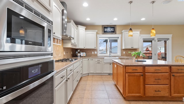 kitchen with backsplash, stainless steel gas cooktop, decorative light fixtures, white cabinetry, and a sink