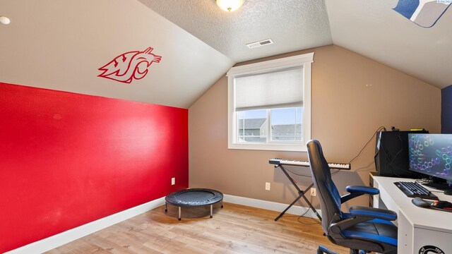 home office featuring wood finished floors, baseboards, visible vents, vaulted ceiling, and a textured ceiling
