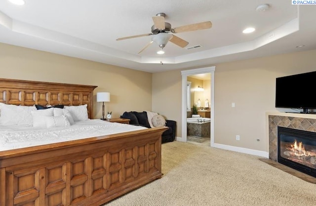 bedroom featuring baseboards, visible vents, a tray ceiling, a tile fireplace, and light colored carpet