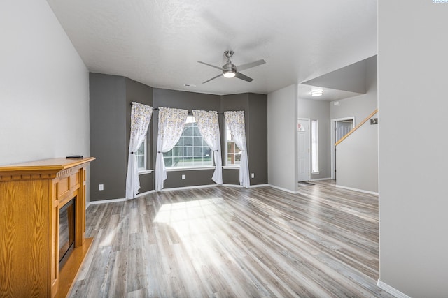 unfurnished living room with ceiling fan, baseboards, wood finished floors, and a glass covered fireplace