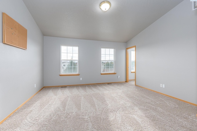 unfurnished room with lofted ceiling, carpet, visible vents, and baseboards