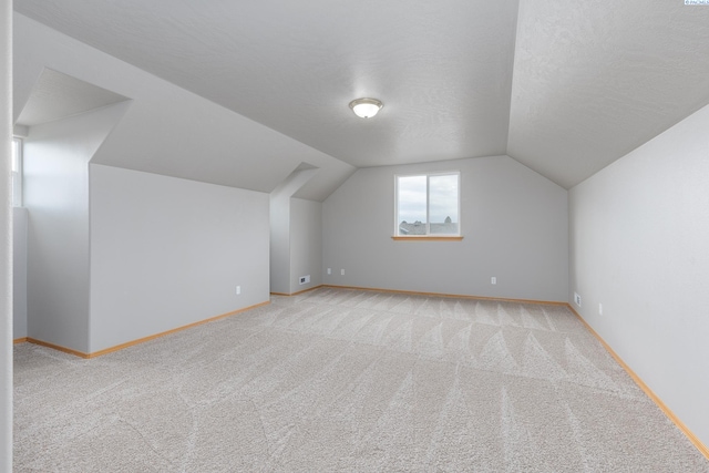 bonus room featuring vaulted ceiling, a textured ceiling, light carpet, and baseboards