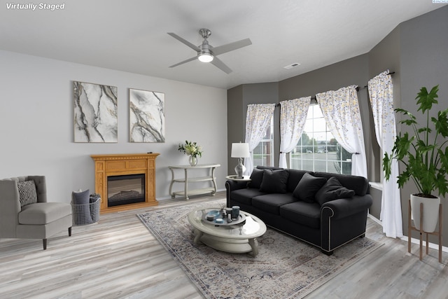 living room featuring light wood-type flooring, baseboards, visible vents, and a glass covered fireplace