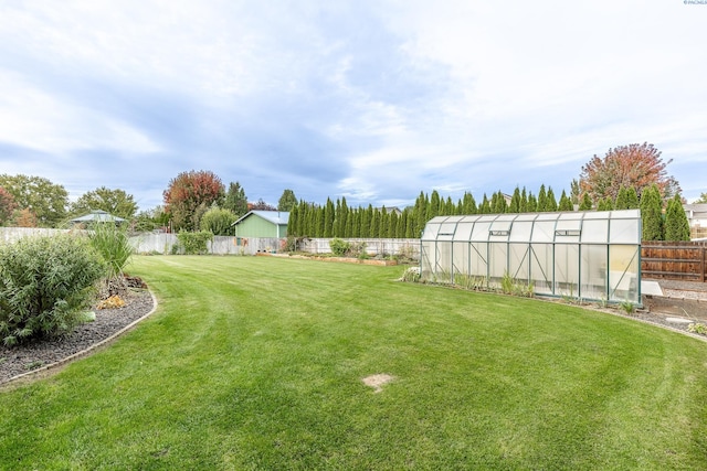 view of yard featuring an outbuilding, a greenhouse, and a fenced backyard