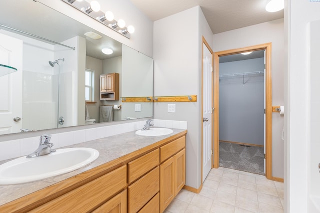 bathroom featuring a spacious closet, double vanity, walk in shower, and a sink