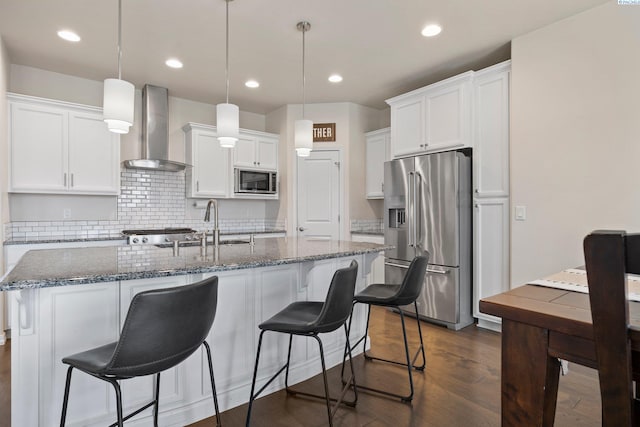 kitchen with white cabinetry, stainless steel appliances, decorative light fixtures, and wall chimney range hood