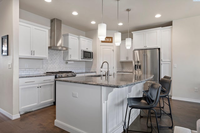 kitchen featuring wall chimney range hood, sink, a kitchen island with sink, white cabinetry, and stainless steel appliances