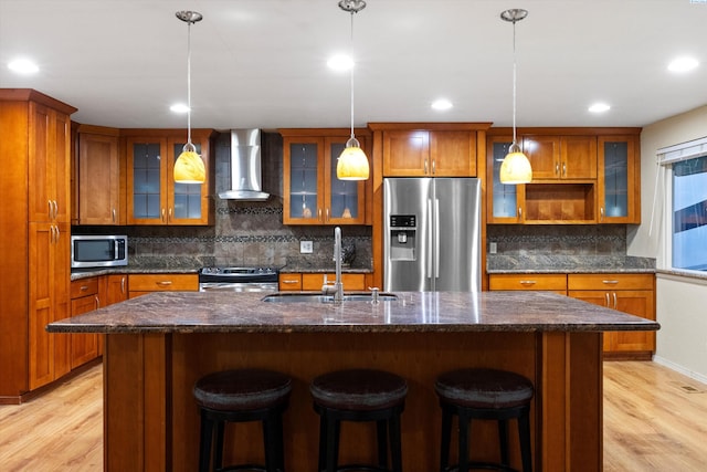 kitchen featuring pendant lighting, sink, stainless steel appliances, a center island with sink, and wall chimney exhaust hood