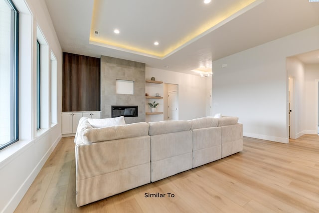 living area with light wood-style flooring, baseboards, recessed lighting, a tile fireplace, and a tray ceiling