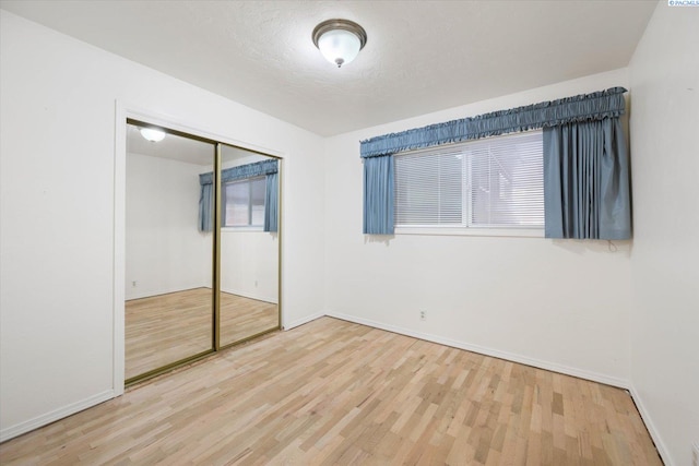 unfurnished bedroom featuring multiple windows, hardwood / wood-style floors, a closet, and a textured ceiling