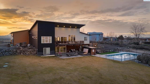 back house at dusk with a fenced in pool, a patio, and a yard