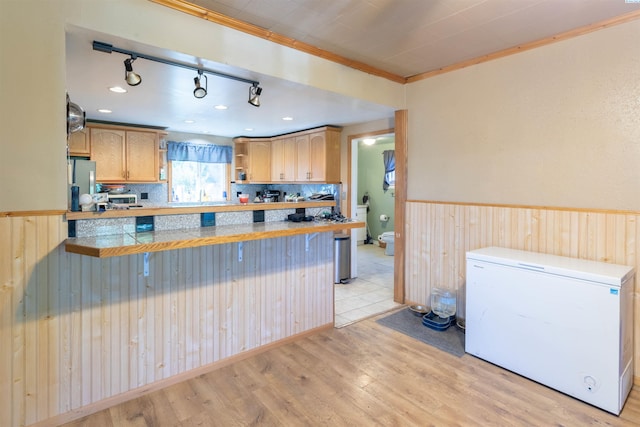 kitchen with white fridge, light wood-style flooring, wainscoting, a peninsula, and wood walls