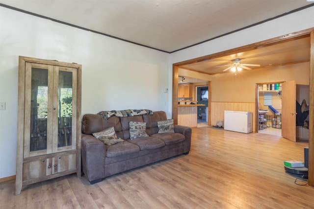 living room featuring wood finished floors, crown molding, a wainscoted wall, and a ceiling fan