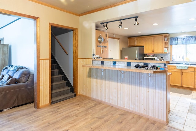kitchen with freestanding refrigerator, ornamental molding, light countertops, a sink, and light wood finished floors
