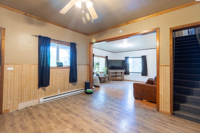 living area with a baseboard radiator, crown molding, stairs, wainscoting, and wood finished floors