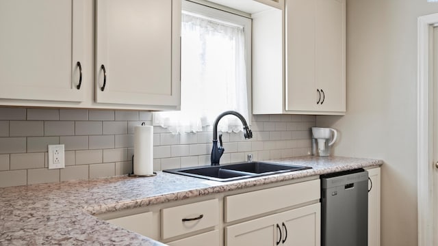 kitchen featuring stainless steel dishwasher, a sink, backsplash, and white cabinets