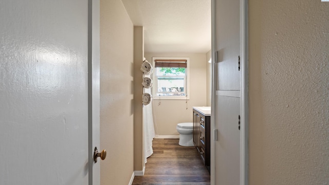 bathroom featuring vanity, a textured wall, wood finished floors, toilet, and baseboards