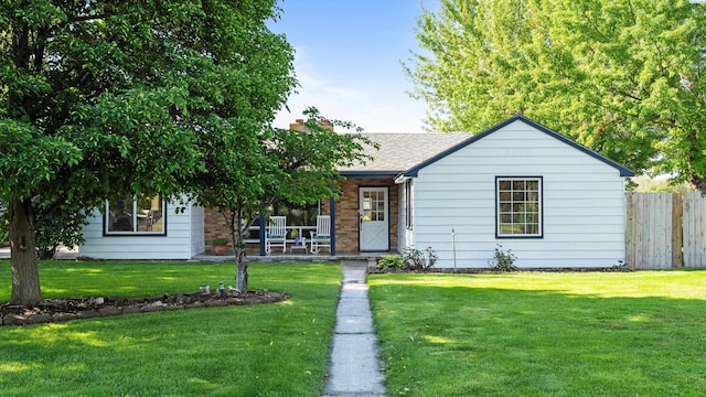 ranch-style home with fence, a shingled roof, a front lawn, brick siding, and covered porch