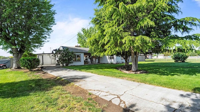 view of property hidden behind natural elements with fence, driveway, and a front yard