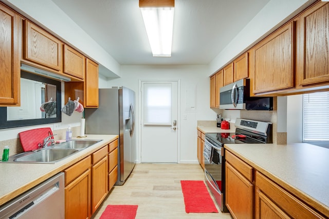 kitchen featuring light wood finished floors, light countertops, appliances with stainless steel finishes, brown cabinetry, and a sink