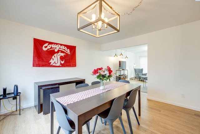 dining space featuring light wood finished floors, baseboards, and a chandelier