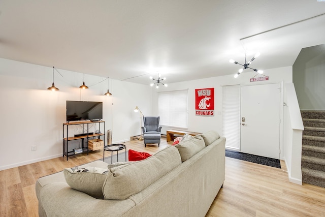 living area featuring light wood-type flooring, an inviting chandelier, stairs, and baseboards