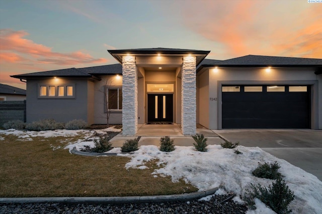 prairie-style house with a yard, stucco siding, an attached garage, stone siding, and driveway