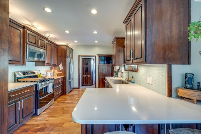 kitchen with a sink, stainless steel appliances, light countertops, dark brown cabinets, and light wood-style floors