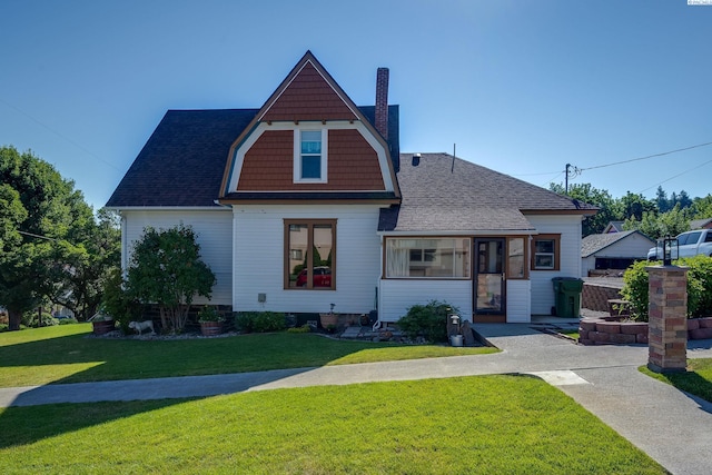 view of front facade featuring a gambrel roof, a chimney, a front lawn, and roof with shingles