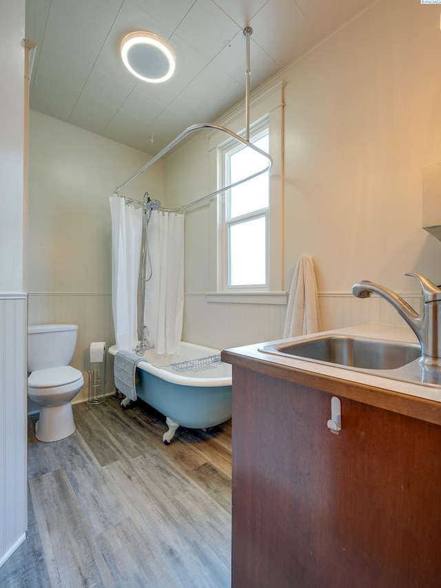 bathroom featuring a wainscoted wall, toilet, shower / tub combo, wood finished floors, and a sink