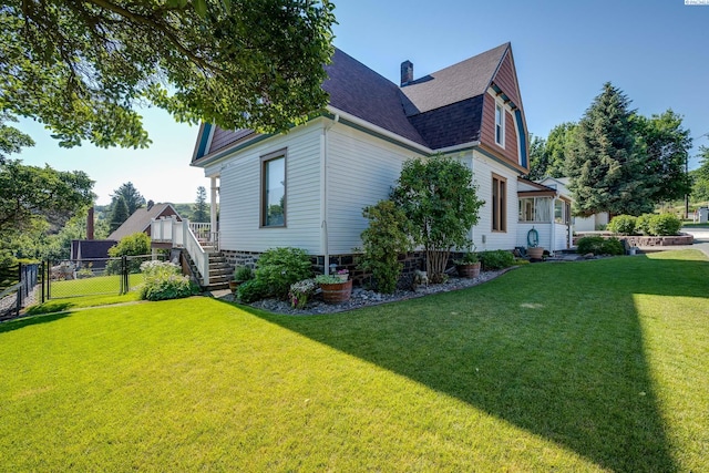 view of property exterior featuring a yard, a gambrel roof, roof with shingles, and fence