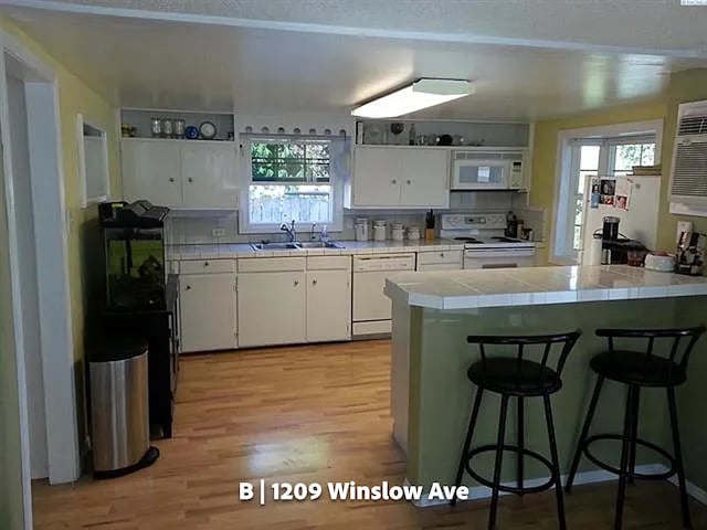kitchen with sink, a breakfast bar area, white cabinetry, tile countertops, and white appliances