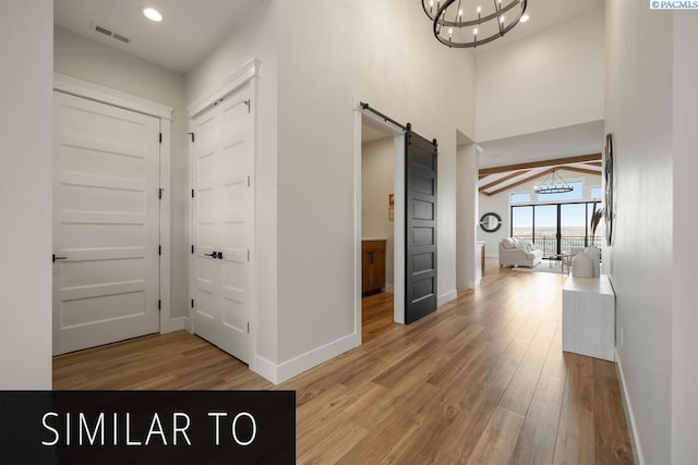 hall featuring hardwood / wood-style flooring, a high ceiling, beam ceiling, a barn door, and an inviting chandelier