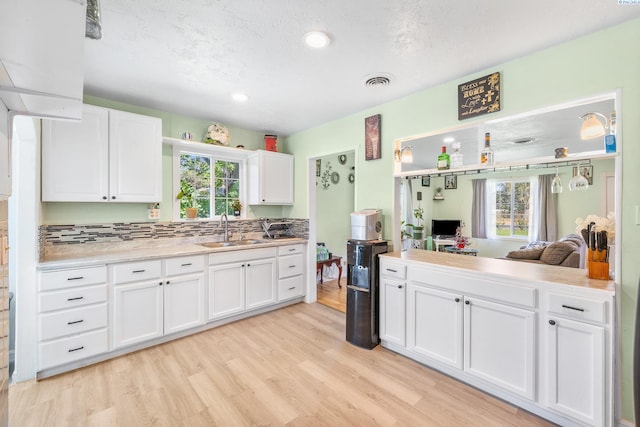 kitchen featuring white cabinetry, sink, light wood-type flooring, and a healthy amount of sunlight