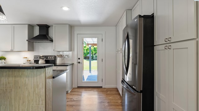 654 Cottonwood Dr, Richland, WA 99352 - kitchen featuring wall chimney range hood, freestanding refrigerator, light wood-style floors, dark countertops, and baseboards