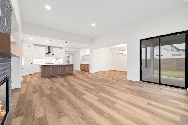 unfurnished living room with sink, a notable chandelier, a fireplace, and light wood-type flooring