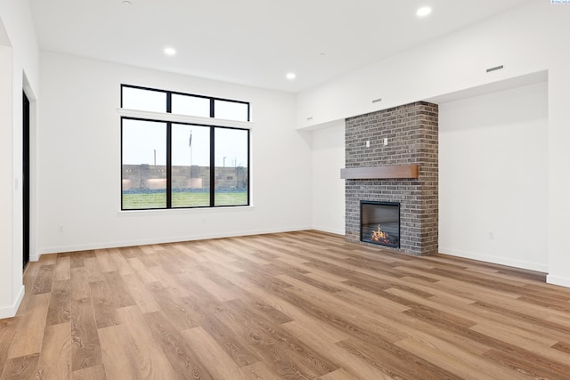 unfurnished living room with light hardwood / wood-style floors and a brick fireplace