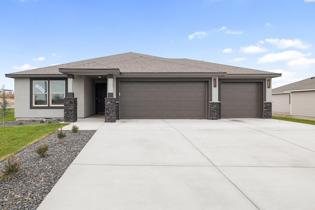 prairie-style house featuring stucco siding, a shingled roof, an attached garage, stone siding, and driveway