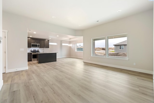 10402 Kokanee Dr, Pasco, WA 99301 - unfurnished living room featuring baseboards, light wood-style flooring, an inviting chandelier, a sink, and recessed lighting