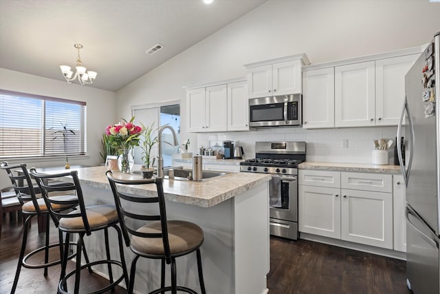 kitchen with stainless steel appliances, an island with sink, white cabinets, decorative light fixtures, and a kitchen bar