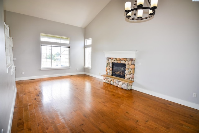 unfurnished living room featuring baseboards, an inviting chandelier, a stone fireplace, hardwood / wood-style flooring, and high vaulted ceiling