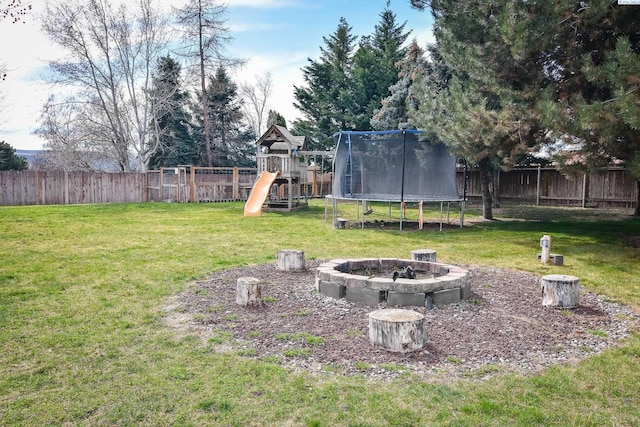 view of yard with a fenced backyard, a trampoline, a fire pit, and a playground