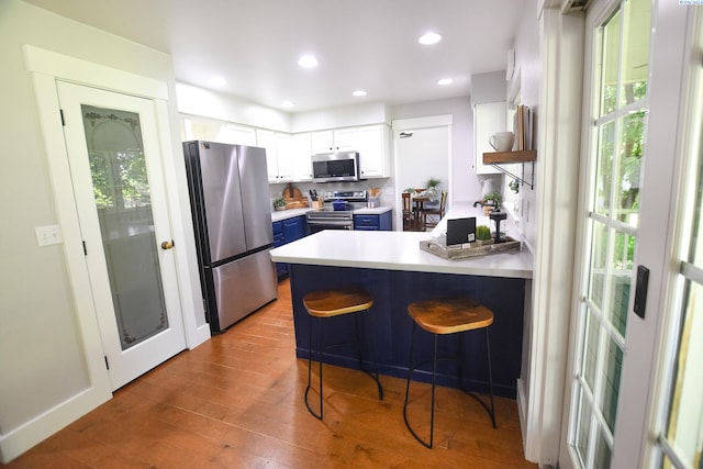 2780 Katie Rd, Kennewick, WA 99338 - kitchen with stainless steel appliances, blue cabinetry, a peninsula, white cabinets, and wood finished floors