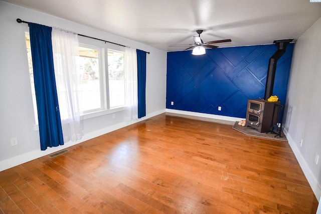 spare room with visible vents, baseboards, a wood stove, a ceiling fan, and hardwood / wood-style flooring