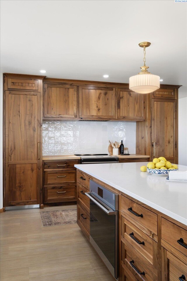 170732 Olsen Rd, Grandview, WA 98930 - kitchen featuring stainless steel oven, backsplash, brown cabinetry, light wood-style flooring, and decorative light fixtures