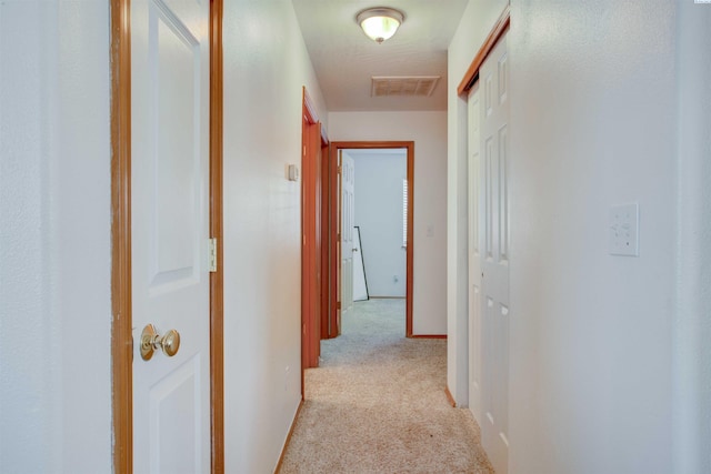 hall featuring light carpet, visible vents, and baseboards