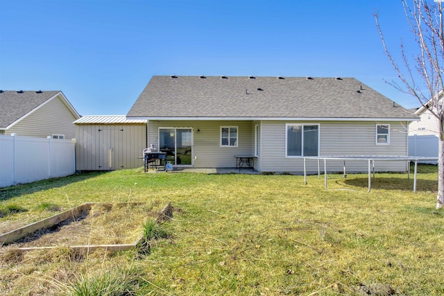 back of house with a shingled roof, a vegetable garden, a lawn, a trampoline, and fence