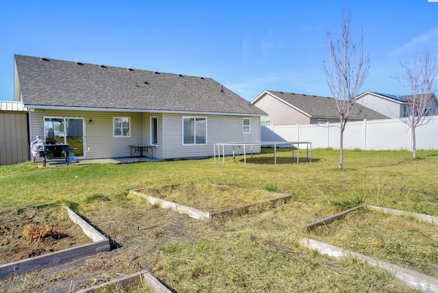 back of property with fence, a yard, roof with shingles, a vegetable garden, and a trampoline